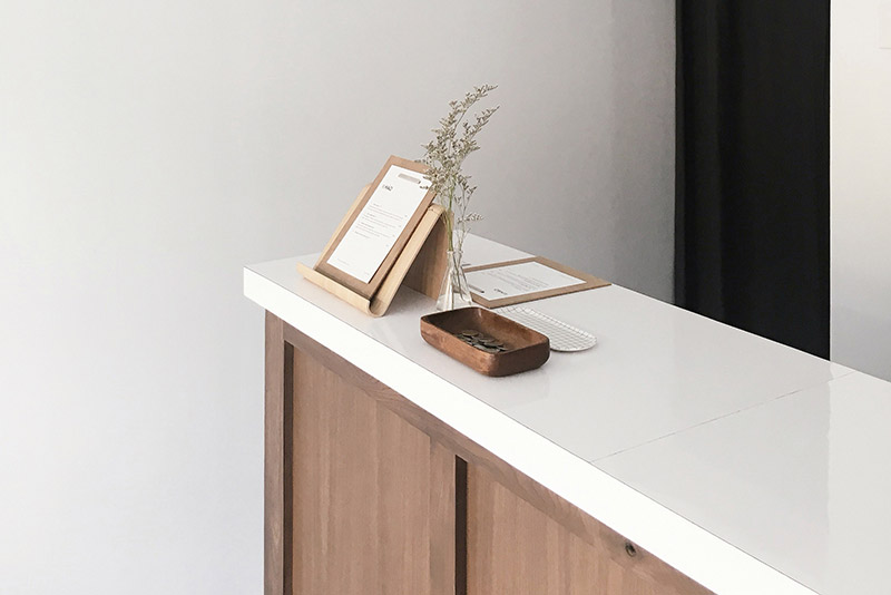 Ile papierosów odpowiada 5000 zaciągnięć? 1 Nowoczesna lada recepcyjna o minimalistycznym, drewnianym designie, prezentująca starannie ułożone karty informacyjne na stojakach, zaakcentowana małym szklanym wazonem zawierającym delikatne suszone rośliny i stylowym drewnianym naczyniem.