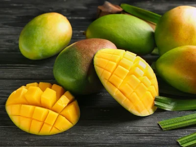 What Are the Most Popular Disposable Vape Flavors in 2026? 5 A group of fresh whole mangoes and a sliced mango with cubed flesh on a dark wooden surface.