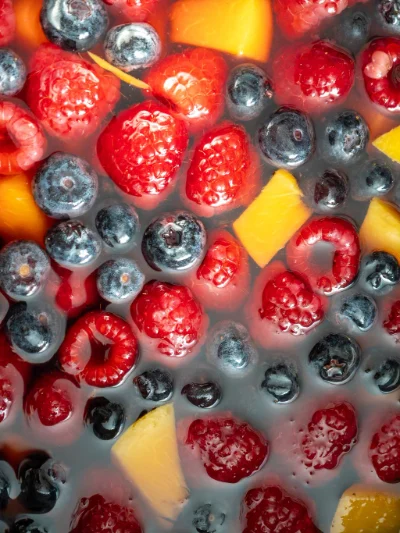 What Are the Most Popular Disposable Vape Flavors in 2026? 9 Top view of mixed berries including raspberries and blueberries, accompanied by slices of peach, submerged in a liquid.
